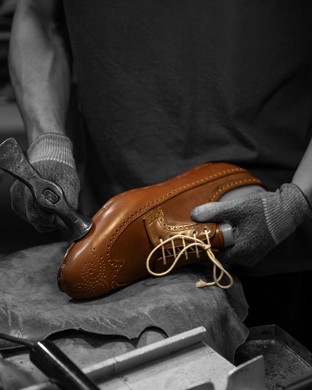 Person holding a brown leather shoe with tools on a dark surface